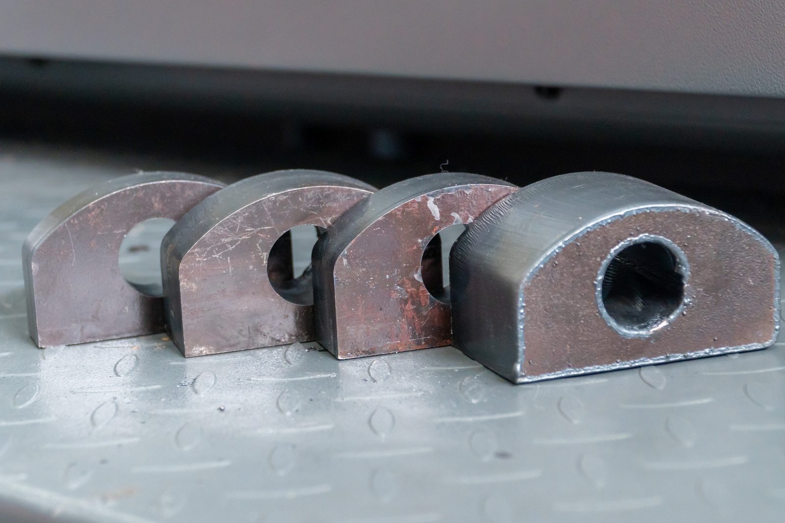Four heavy steel sections with laser-cut radii and bores, set out on a workshop floor